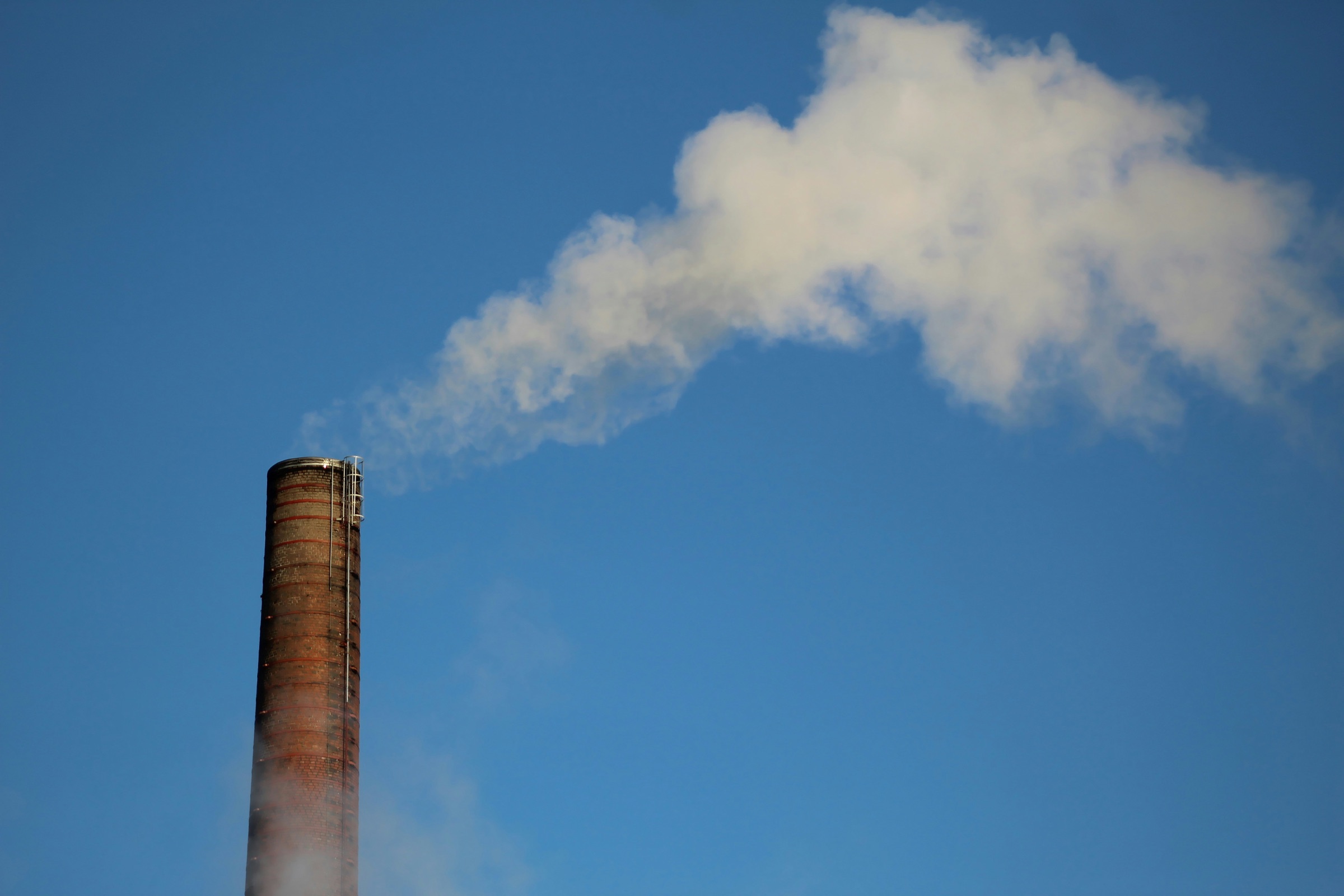 A brick smokestack releasing a plume of white smoke into a blue sky